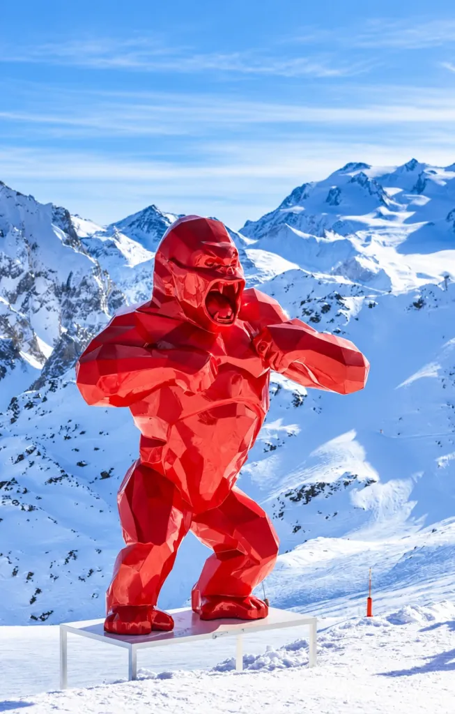 A large red faceted Wild Kong sculpture on a snowy mountain slope above Courchevel 1850