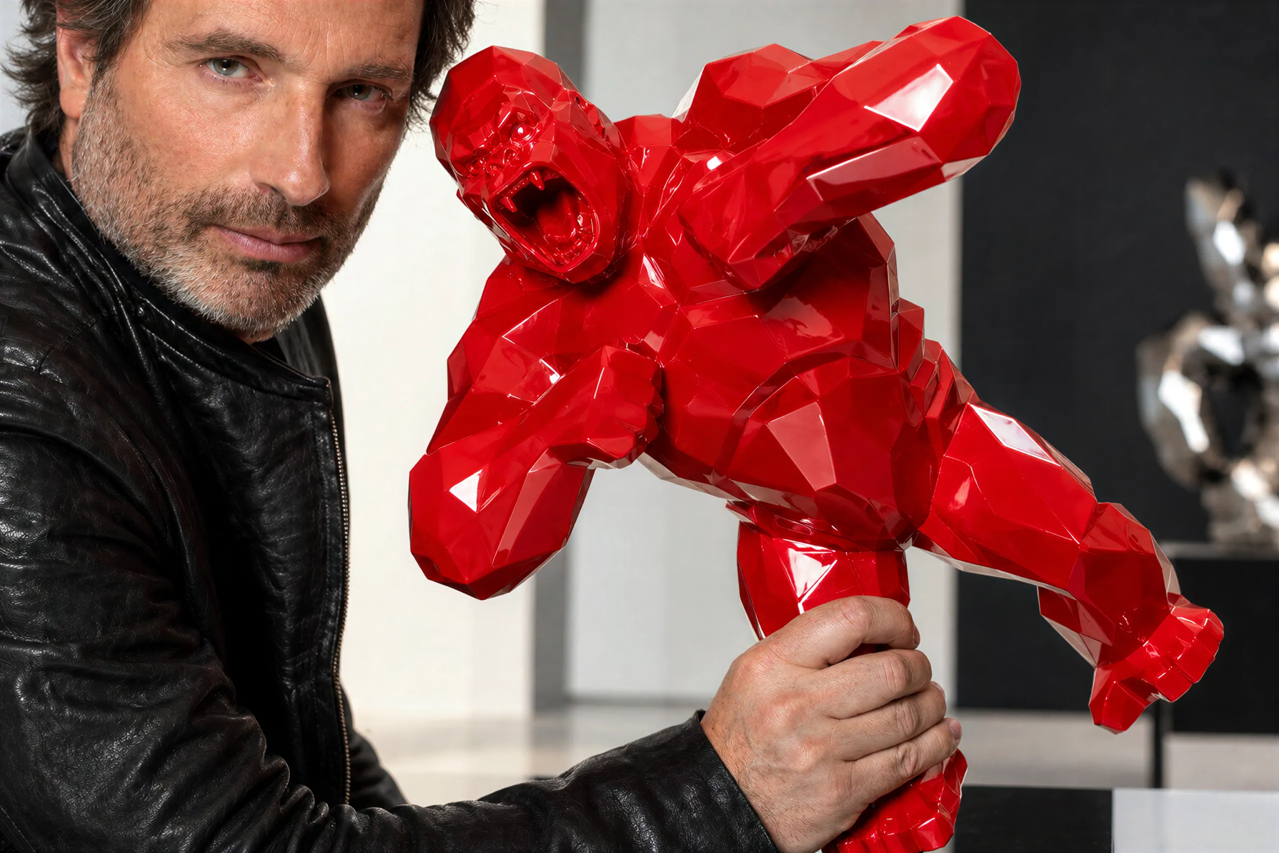 Richard Orlinski in a black leather jacket holding a small red faceted Wild Kong sculpture in a gallery